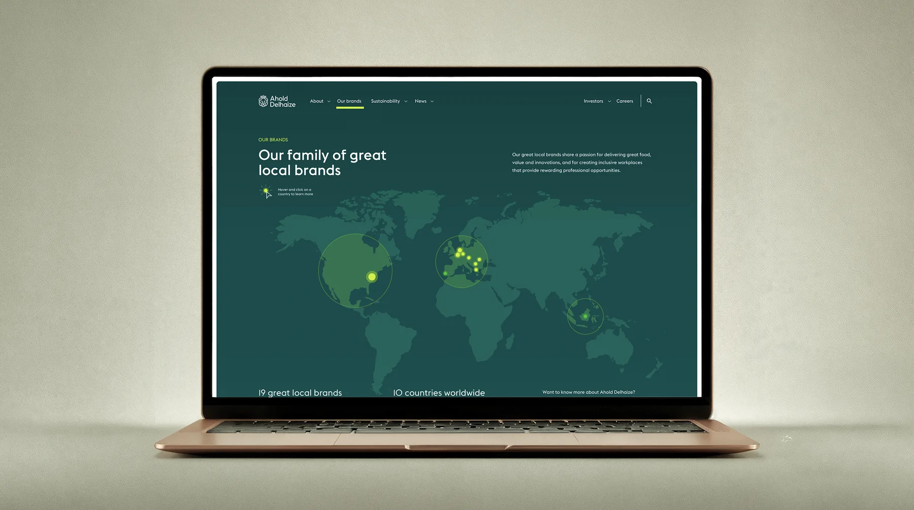 A laptop on a soft greige backdrop showing the redesigned Ahold Delhaize brands page: "Our family of great local brands" over a world map with brand locations