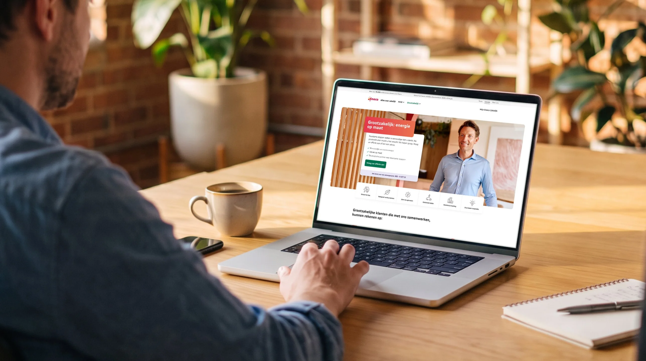 A business owner at a warm wooden desk viewing the redesigned Eneco Zakelijk website on a laptop